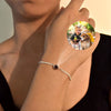Una mujer lleva la Pulsera Recuerdo eterno con una piedra oscura; un inserto circular encima muestra la imagen de un niño y un perro, destacando esta pulsera personalizada como un regalo único que esconde tu foto especial en su interior.