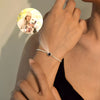 Una mujer lleva la Pulsera Recuerdo eterno con un amuleto circular negro que proyecta una pequeña foto de una mujer sonriente con gorro abrazando a su perro blanco, brillando suavemente cerca de su muñeca.