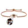 Pulsera Recuerdo eterno en oro rosa, ajustable, con un dije redondo que oculta una foto personalizada de una pareja con su bebé; detalle ampliado en la imagen. Un regalo memorable y personalizado.