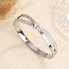 La Pulsera Riviera es una pulsera brazalete de acero inoxidable plateado con números romanos grabados y dos filas de circonitas brillantes, que se muestran sobre una superficie de textura ligera.