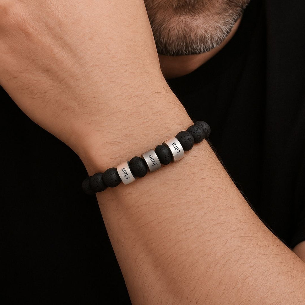 Primer plano de la muñeca de un hombre que lleva una Pulsera tejida personalizada con nombres, con cuentas negras y cuentas de nombre grabadas en plata; va vestido con una camisa negra.
