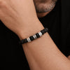 Primer plano de la muñeca de un hombre que lleva una Pulsera tejida personalizada con nombres, con cuentas negras y cuentas de nombre grabadas en plata; va vestido con una camisa negra.