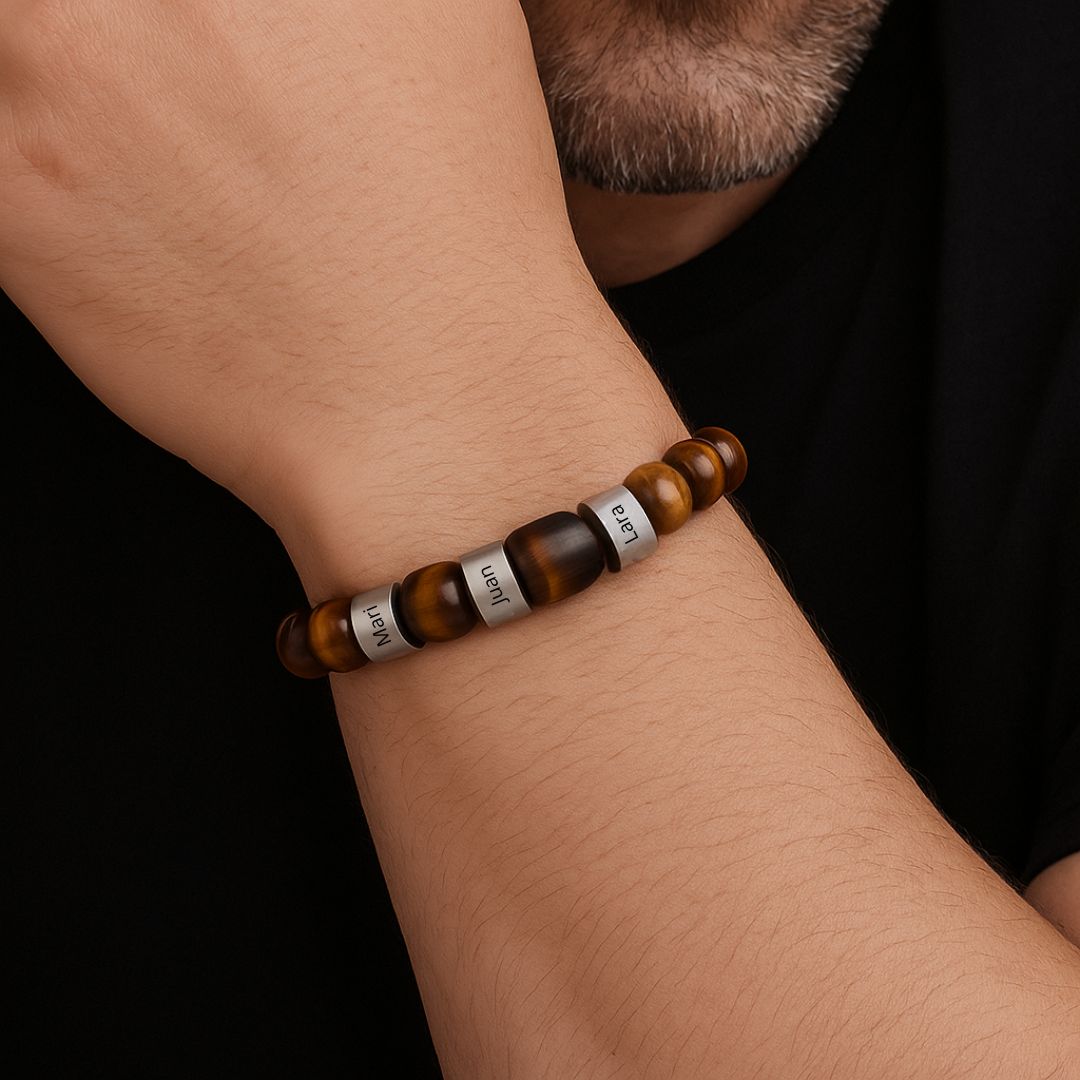 Primer plano de una muñeca que lleva una Pulsera tejida personalizada con nombres con cuentas marrones y plateadas, algunas grabadas. La persona, que tiene vello facial, apoya la barbilla en el brazo para resaltar esta pulsera personalizada para papá.