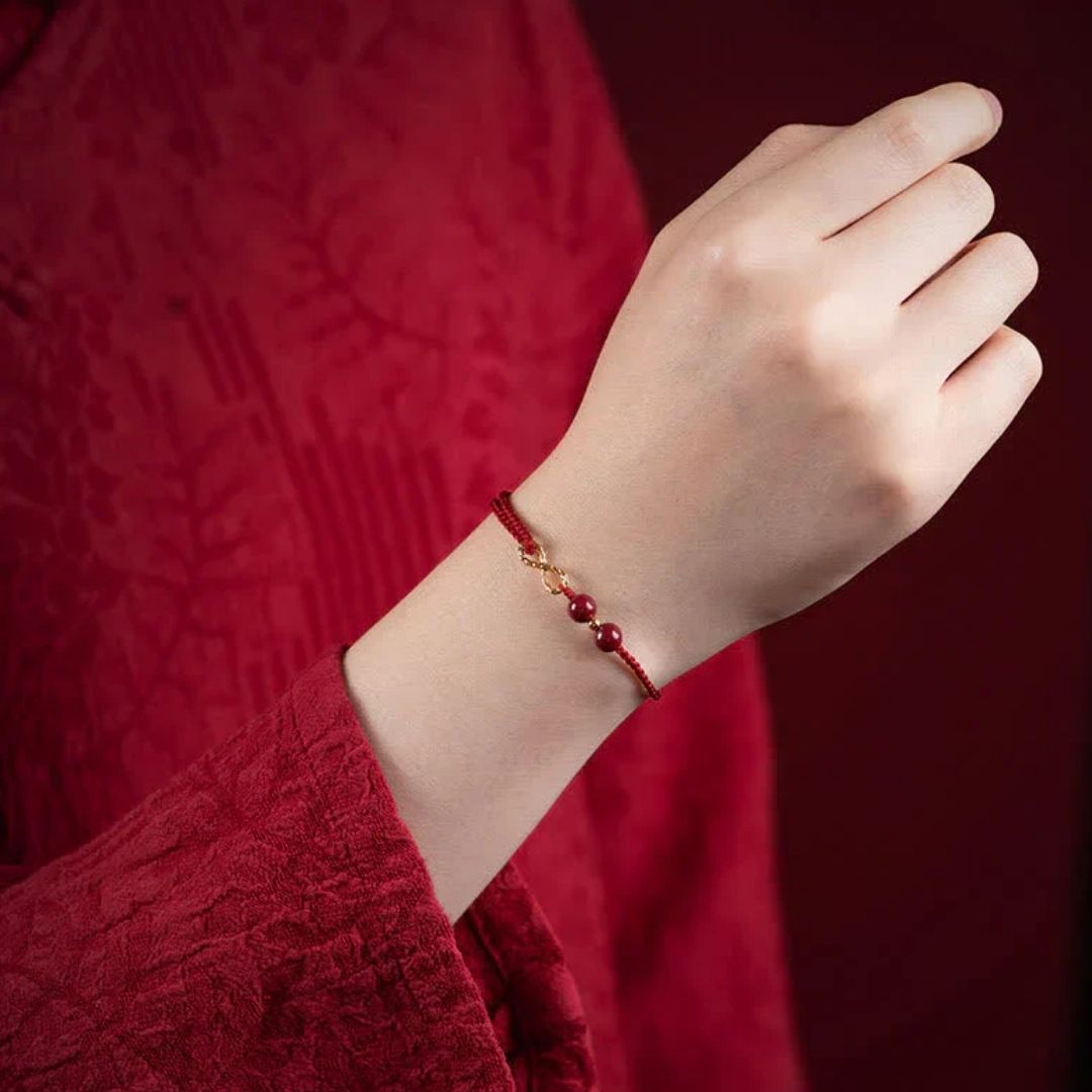 Una mano lleva una Pulsera de amor infinito - Para Él y para Ella, con cuentas doradas y rojas, vestida con tela roja texturizada y sobre un fondo rojo a juego.