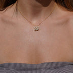 Una mujer lleva el collar "Regalo especial - Rosa eterna y collar 'A mi hija'", cuyo colgante dorado descansa sobre su top gris de tirantes y canalé.