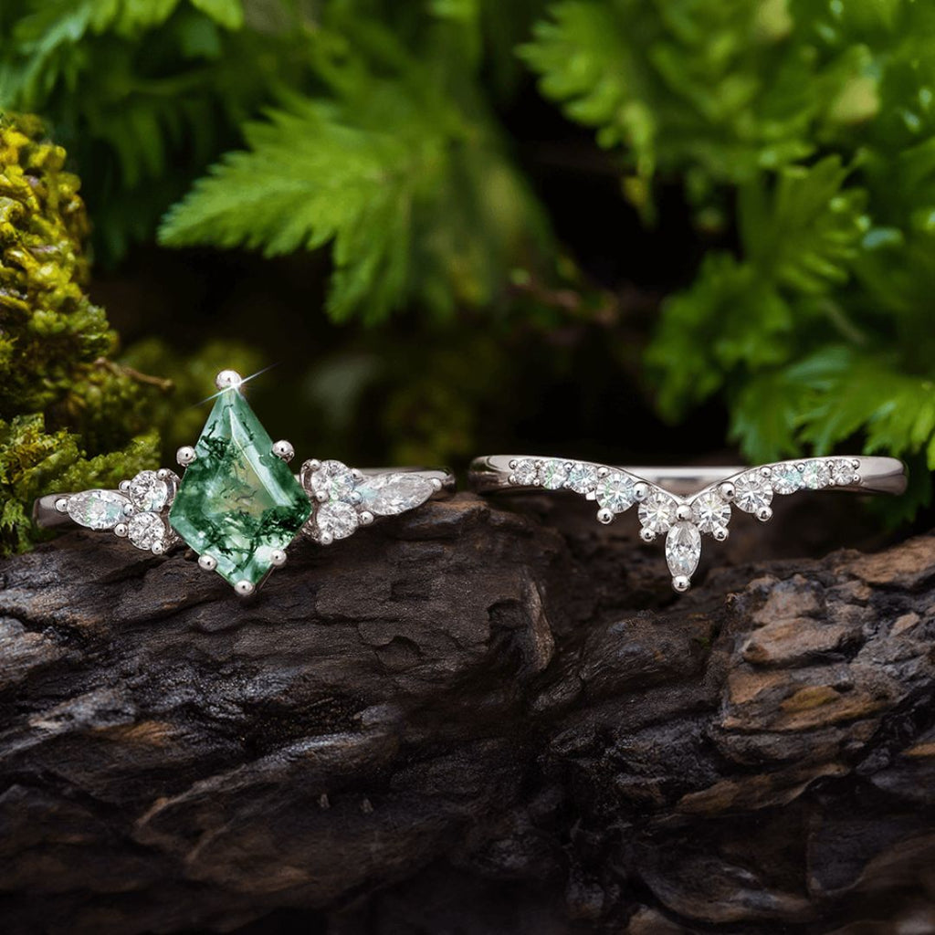 Sobre madera oscura, el Set de anillos piedra ágata verde resalta: uno de compromiso con piedra verde y diamantes blancos, y otro curvo con pequeños diamantes. Follaje natural enmarca este elegante conjunto de anillos.