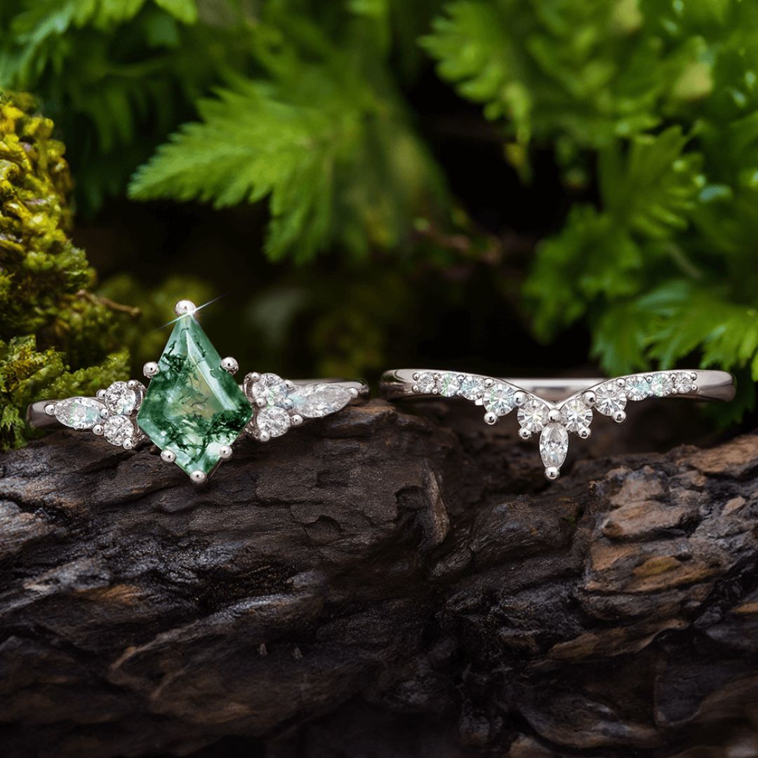 Sobre madera oscura, el Set de anillos piedra ágata verde resalta: uno de compromiso con piedra verde y diamantes blancos, y otro curvo con pequeños diamantes. Follaje natural enmarca este elegante conjunto de anillos.