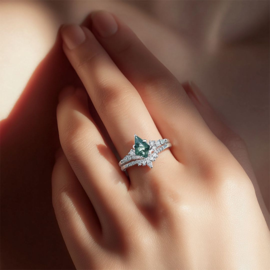Una mano con las uñas cuidadas luce el Set de anillos piedra ágata verde, con una gema verde en forma de triángulo y pequeñas piedras transparentes, bajo una suave luz natural.