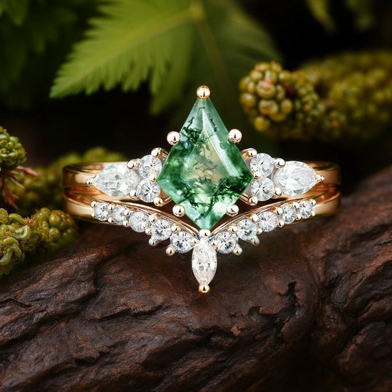 El Set de anillos piedra ágata verde en dorado exhibe una gran piedra central y detalles brillantes, posado sobre madera con follaje verde al fondo.