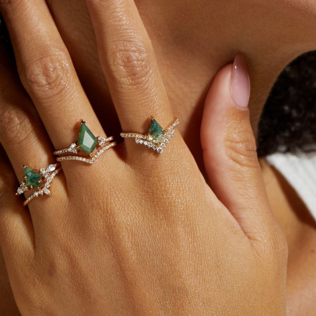 Primer plano de una mano que lleva el Set de anillos piedra ágata verde -tres anillos de oro con piedras de ágata verde y pequeños diamantes- en los dedos índice, corazón y anular. Las uñas están cuidadas en un tono rosa natural.