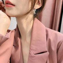 Cargar imagen en el visor de la galería, Primer plano de una mujer vestida con un blazer rosa rubor y el Set de aretes brillantes, con la barbilla apoyada en la mano mientras una suave luz natural resalta su rostro y su pelo.