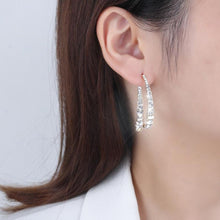 Cargar imagen en el visor de la galería, Primer plano de una mujer que lleva el Set de aretes brillantes, unos brillantes pendientes curvados de acero inoxidable plateado con cristales. Mostrada de perfil sobre un fondo claro, lleva el pelo castaño liso recogido detrás de la oreja.