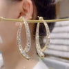 Primer plano de una mujer que lleva el Set de aretes brillantes en color dorado, con incrustaciones de piedras centelleantes. El fondo suavemente difuminado resalta los brillantes pendientes.