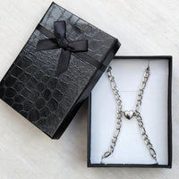 El set de pulseras con corazón magnético, ideal como pulsera de promesa, se presenta en una elegante caja de regalo negra con lazo y patrón texturizado, colocada sobre una superficie clara.