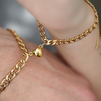 Un primer plano muestra un Set de pulseras con corazón magnético en color dorado en la muñeca, destacando sus eslabones brillantes y el charm de corazón-un detalle ideal como regalo para parejas.