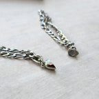 Primer plano de dos cadenas de plata con extremos en forma de bala, sobre madera clara. Este set de pulseras con corazón magnético brilla con eslabones intrincados: un regalo ideal para parejas.