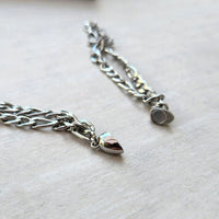 Primer plano de dos cadenas de plata con extremos en forma de bala, sobre madera clara. Este set de pulseras con corazón magnético brilla con eslabones intrincados: un regalo ideal para parejas.