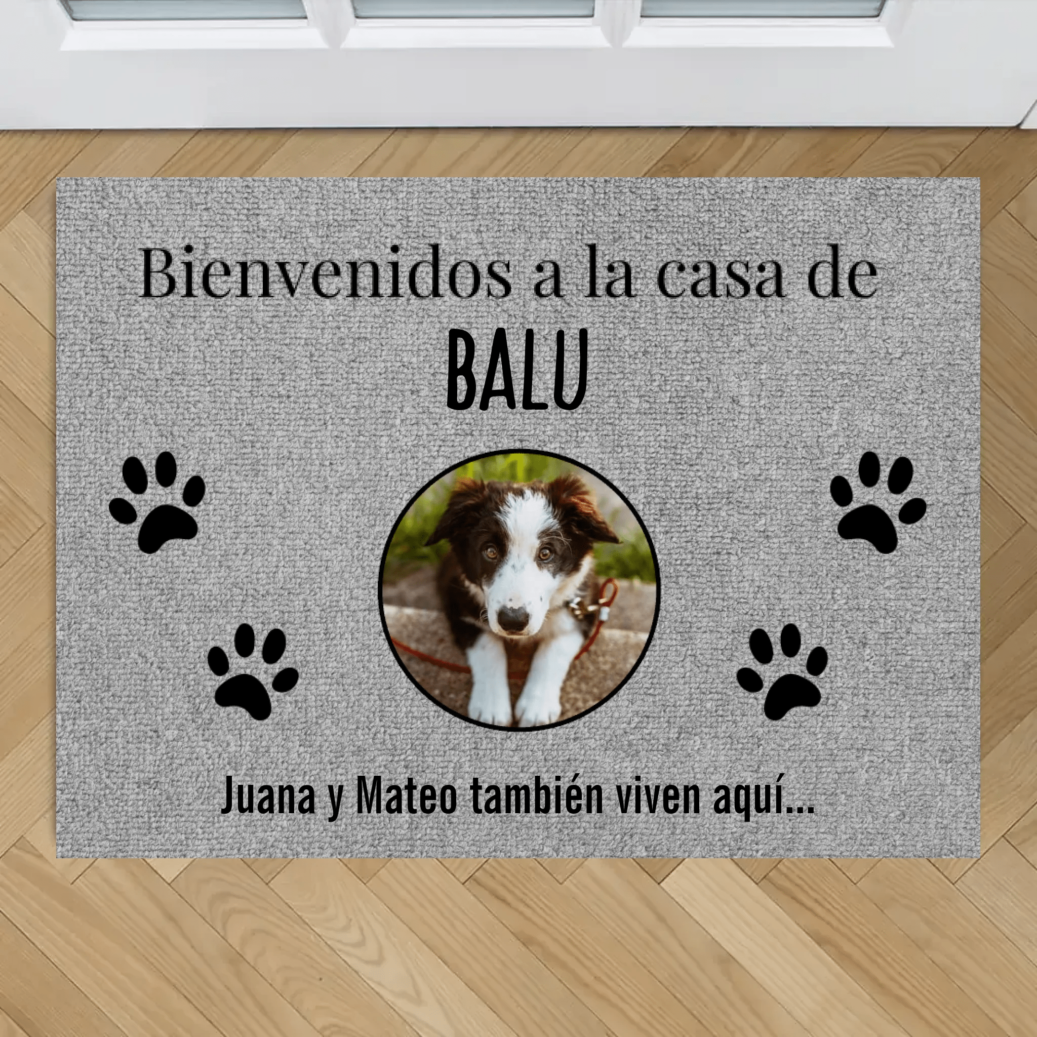 Tapete personalizado con fotos de mascotas: tapete color gris con huellas negras y foto de perro marrón y blanco en el centro. Texto: "Bienvenidos a la casa de BALU. Juana y Mateo también viven aquí...". Ideal para mascotas.